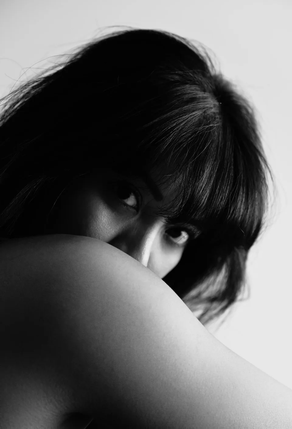 Black-and-white portrait of a woman looking over her bare shoulder, her eyes framed by her fringe