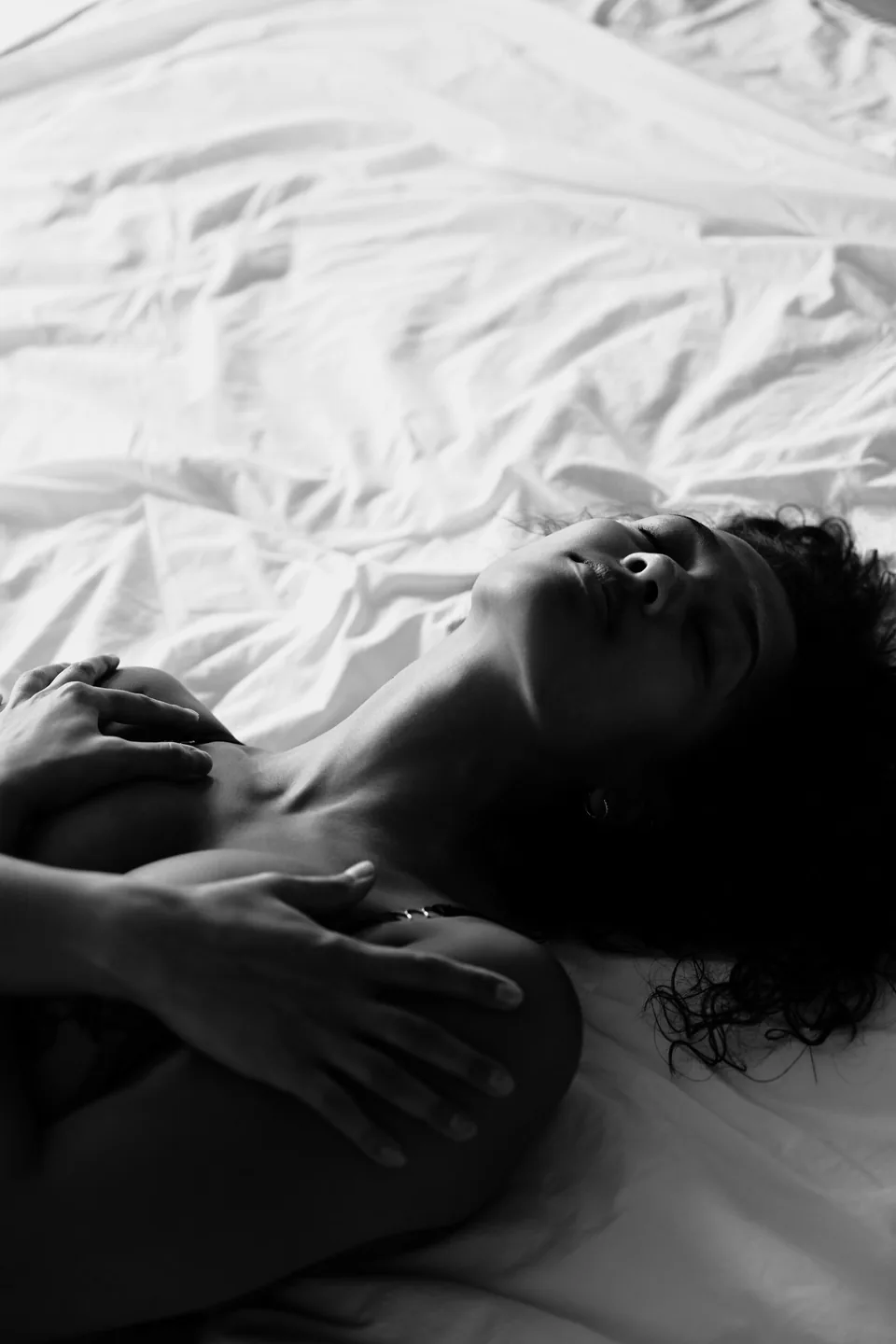 Woman on white sheets, arms crossed over her chest, face turned to the light